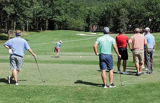 group of male golfers watching golfer hit