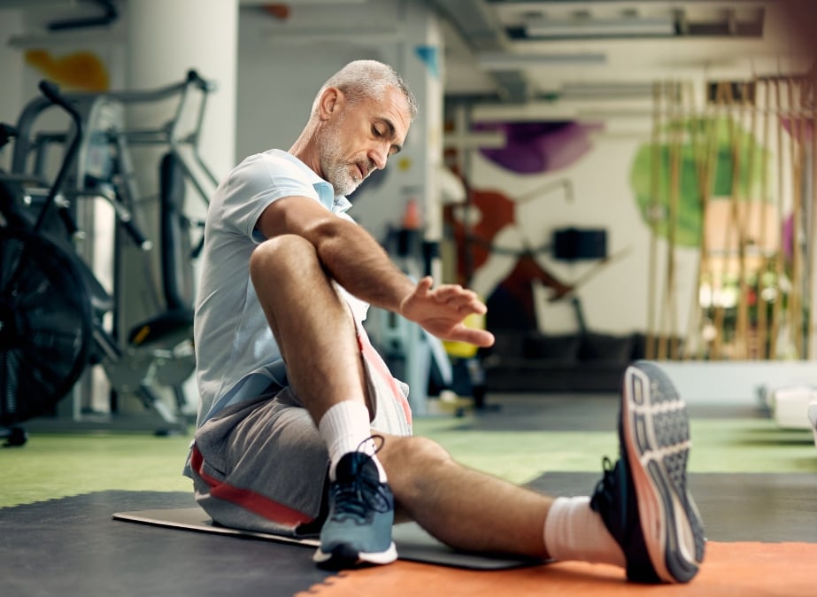 older man doing a leg and abdominal stretch as part of his golf workout regimen 